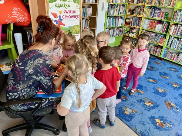 Dzieci z bibliotekarzem oglądają książki dla dzieci 